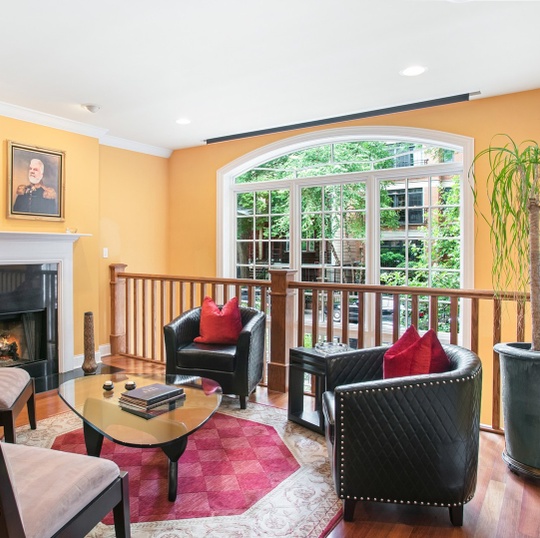 Living room with black leather chairs, a fireplace, and a large arched garden-view window.